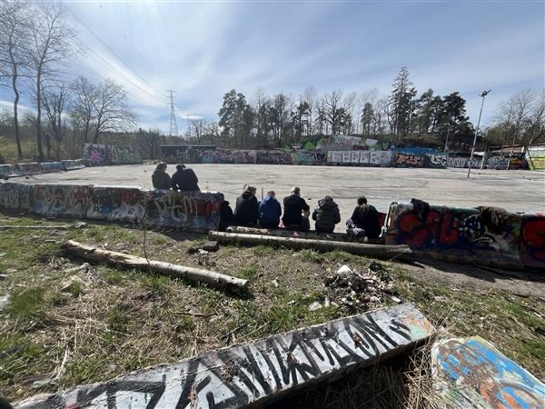 Deltagarna sitter samlade på en mur i graffitiparken och lyssnar